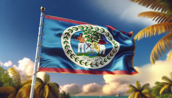 A vibrant Belize flag with detailed coat of arms, waving against a clear sky in lush tropical scenery.